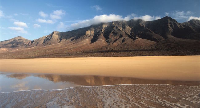 Uitgestrekt strand met op de achtergrond het vulkaanlandschap van Fuerteventura op de Canarische eilanden